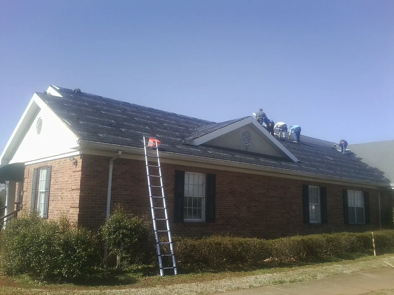 Crew tearing shingles off a brick ranch roof with a ladder set — Emergency Roof Repair work by our crew in Medinah