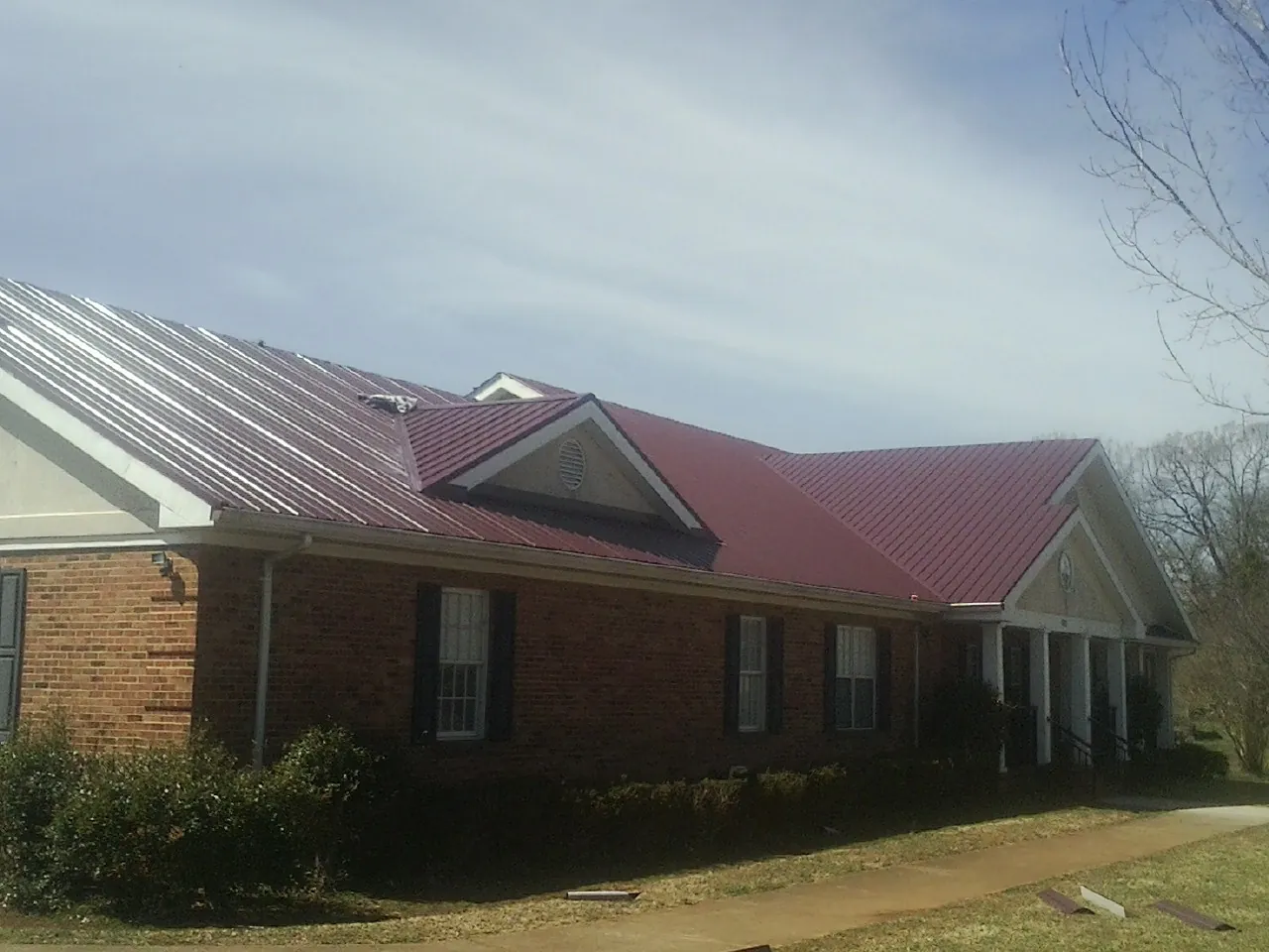 Red metal roof with gabled entries on a long brick building, from a Hail Damage Roof Repair job in Medinah