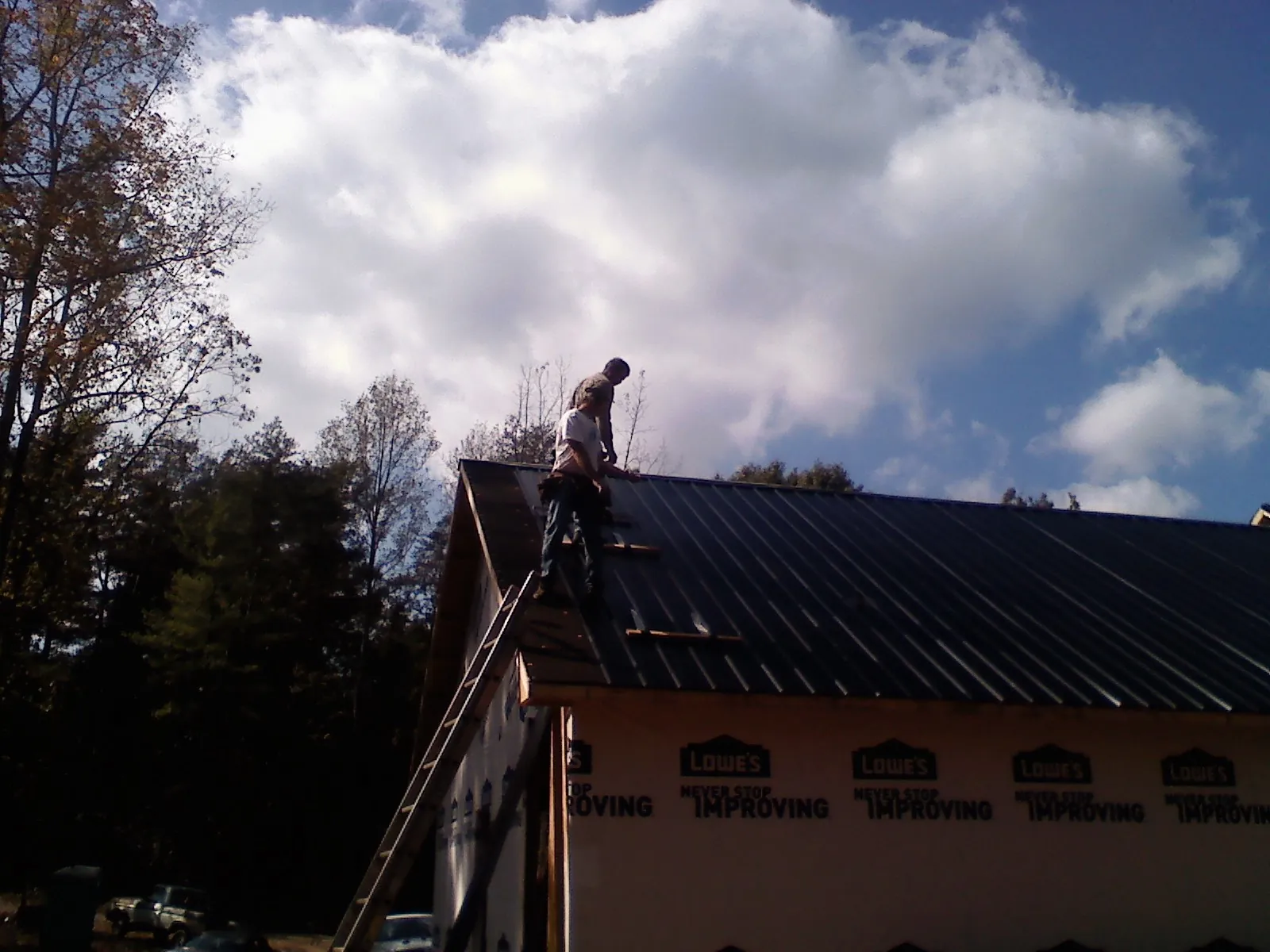 Roofer fastening dark metal panels high against a cloudy sky, from a Roof Inspection job in Medinah