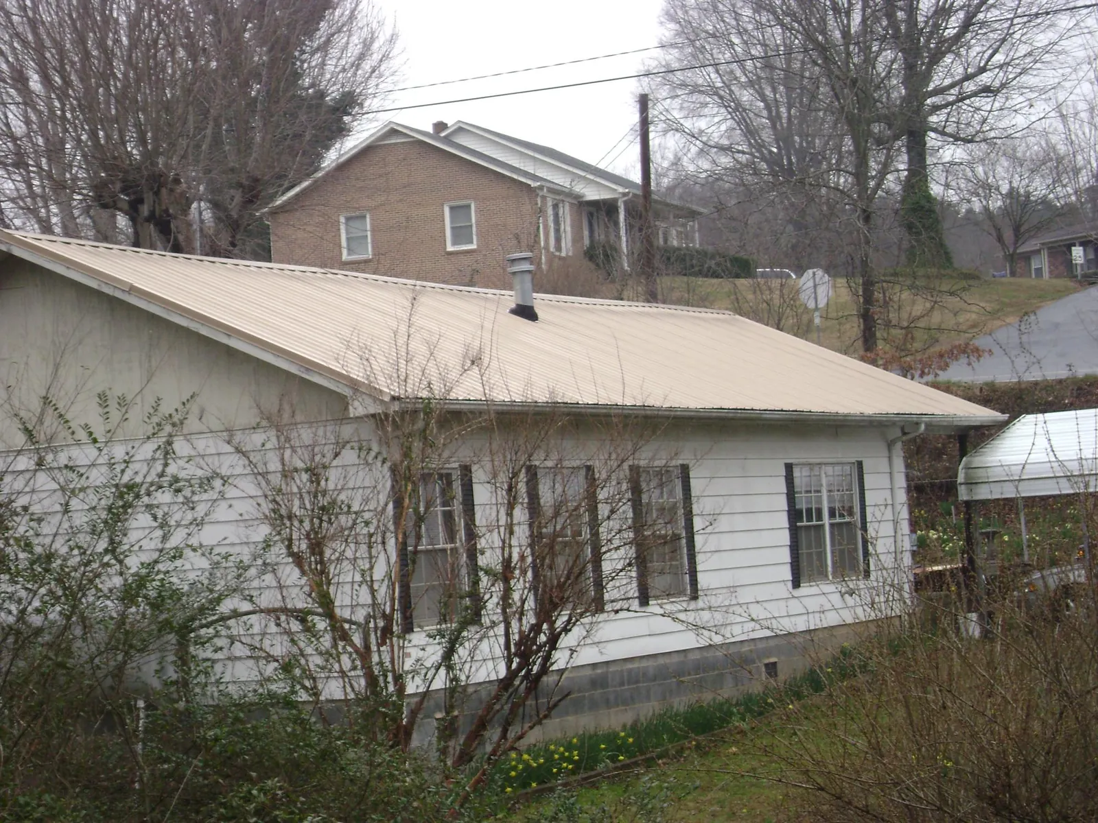 Tan metal roof on a white sided house set into a hillside — Commercial Roofing by Roofing Brothers in Medinah